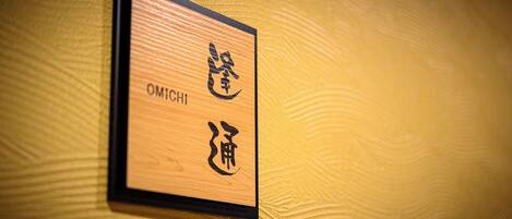 Ein Schild mit japanischen Schriftzeichen und dem Wort 'OMICHII' an einer strukturierten Wand.