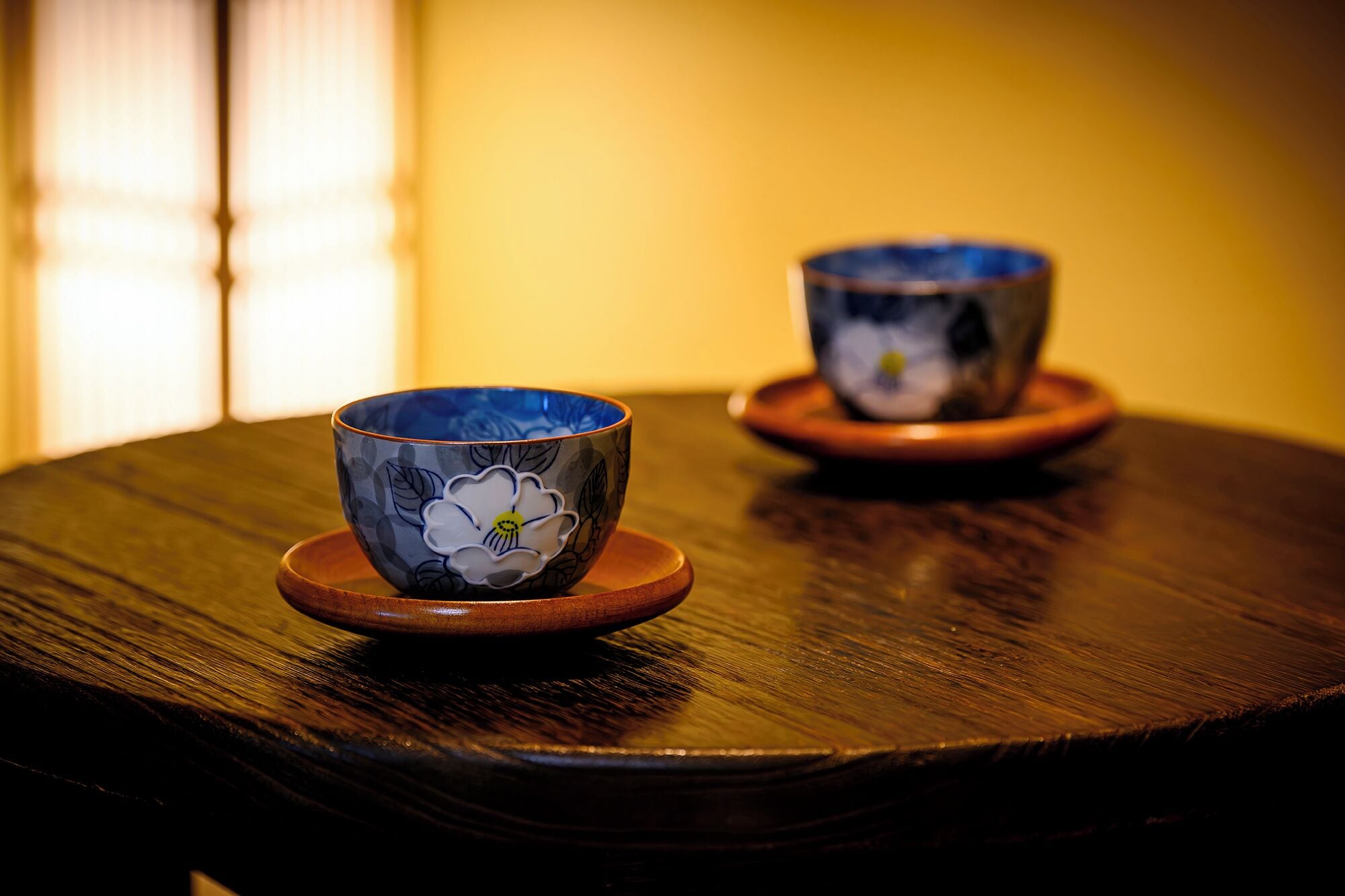 Two ceramic cups with floral designs on a wooden table.