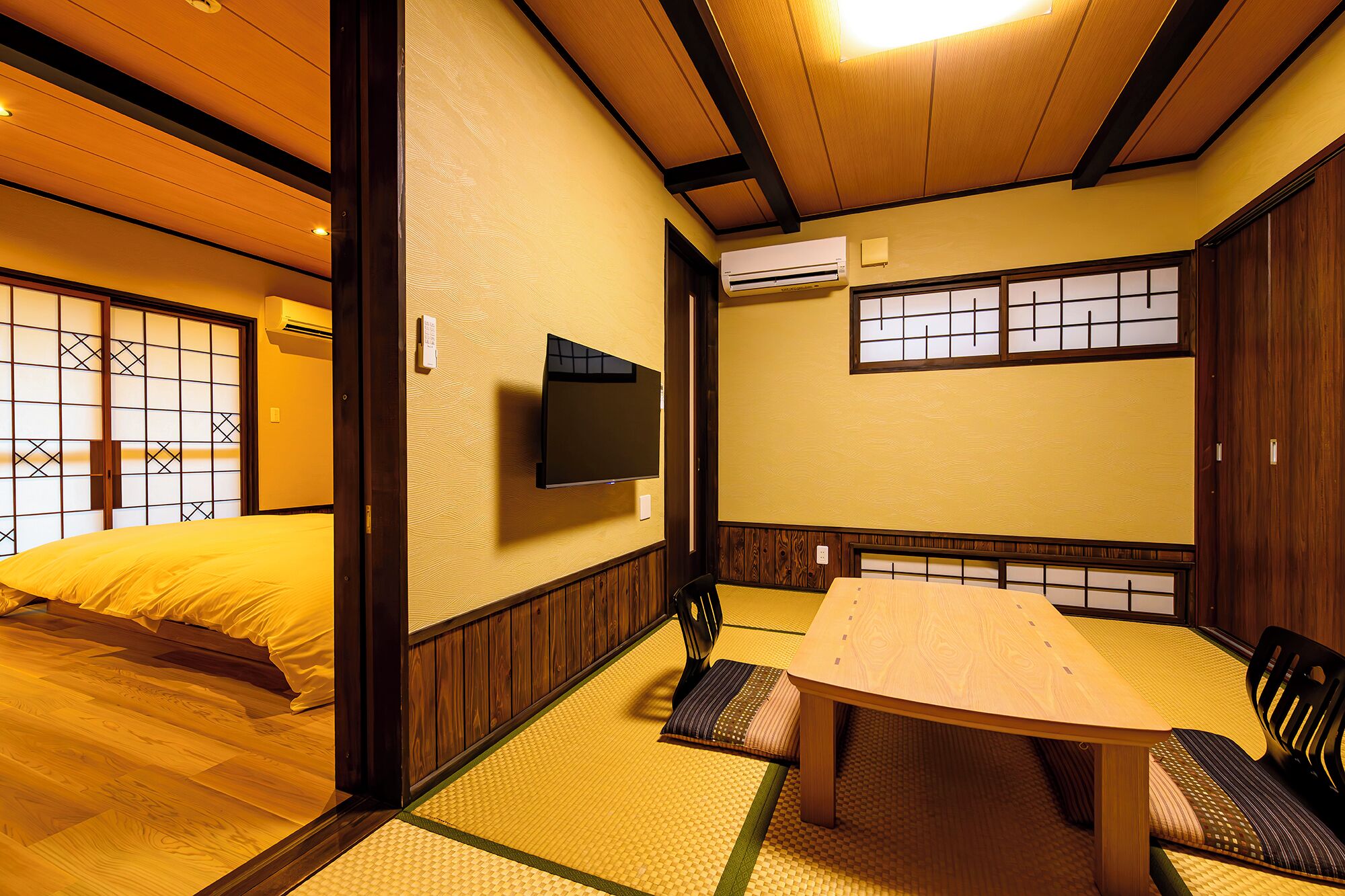 A traditional Japanese room with tatami flooring, a low table, and a TV mounted on the wall.