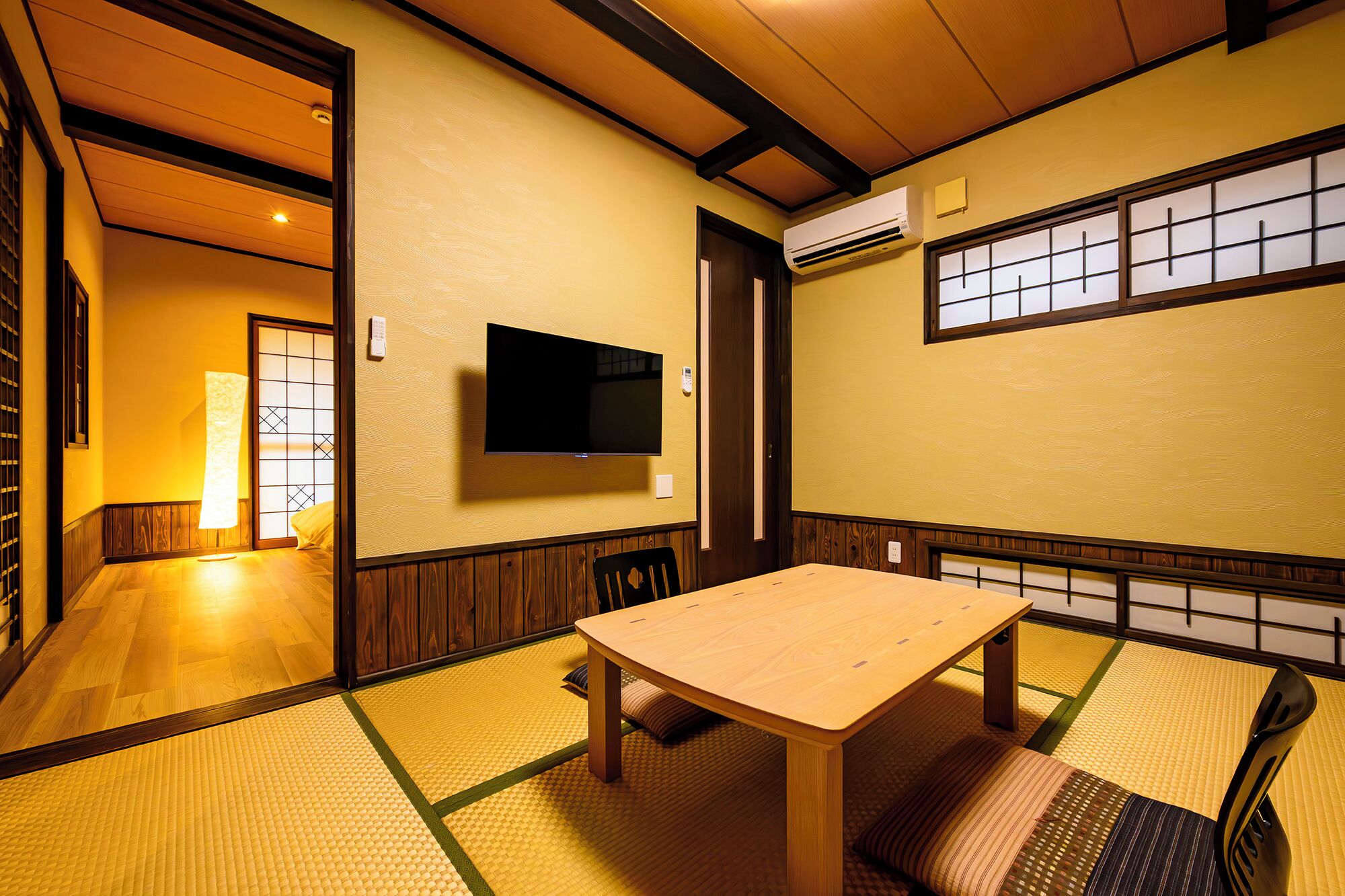A traditional Japanese room with tatami flooring, a low table, and a television mounted on the wall.