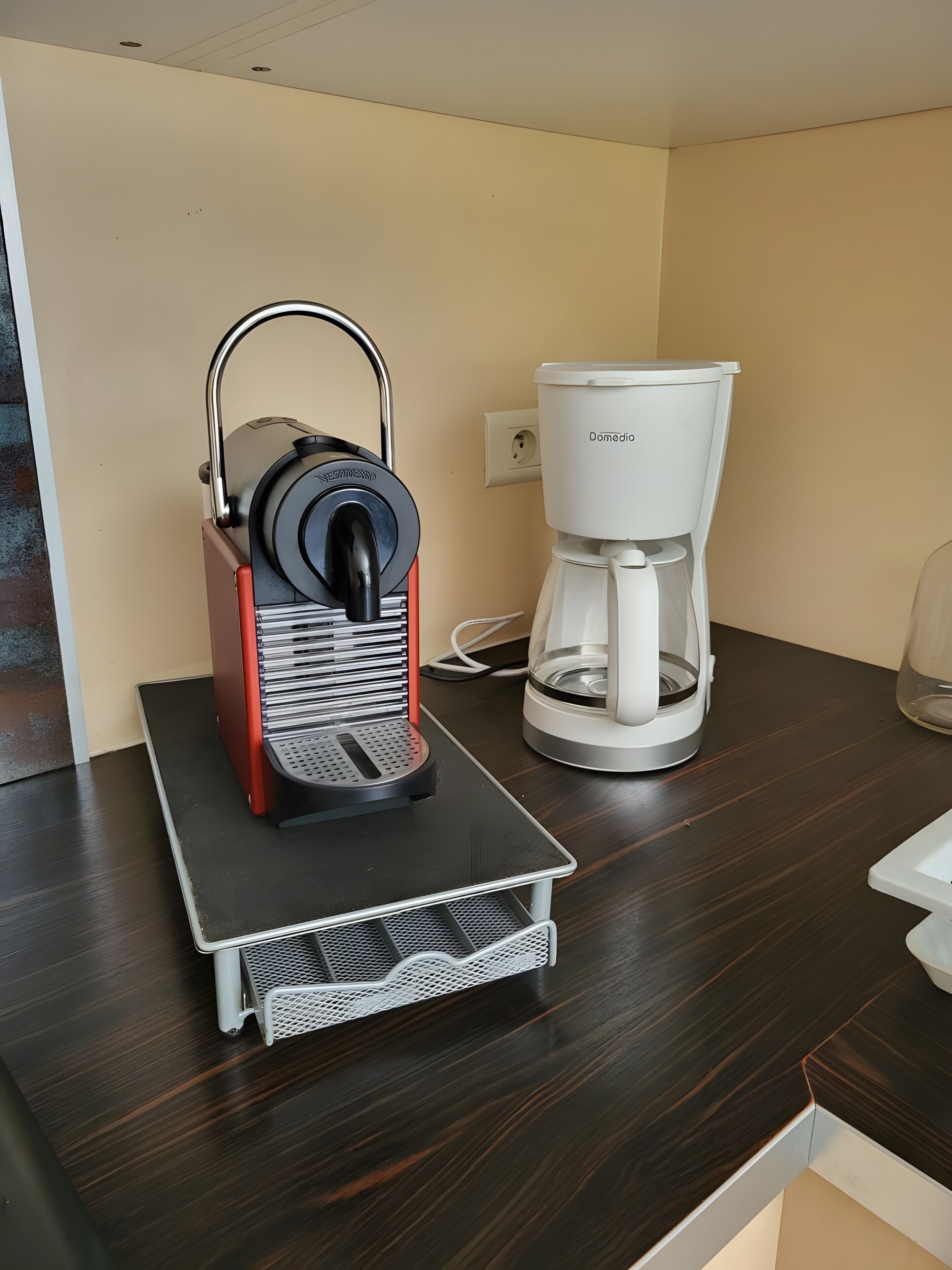 Eine Kaffeemaschine auf einer Arbeitsplatte, daneben eine weiße Kaffeekanne.