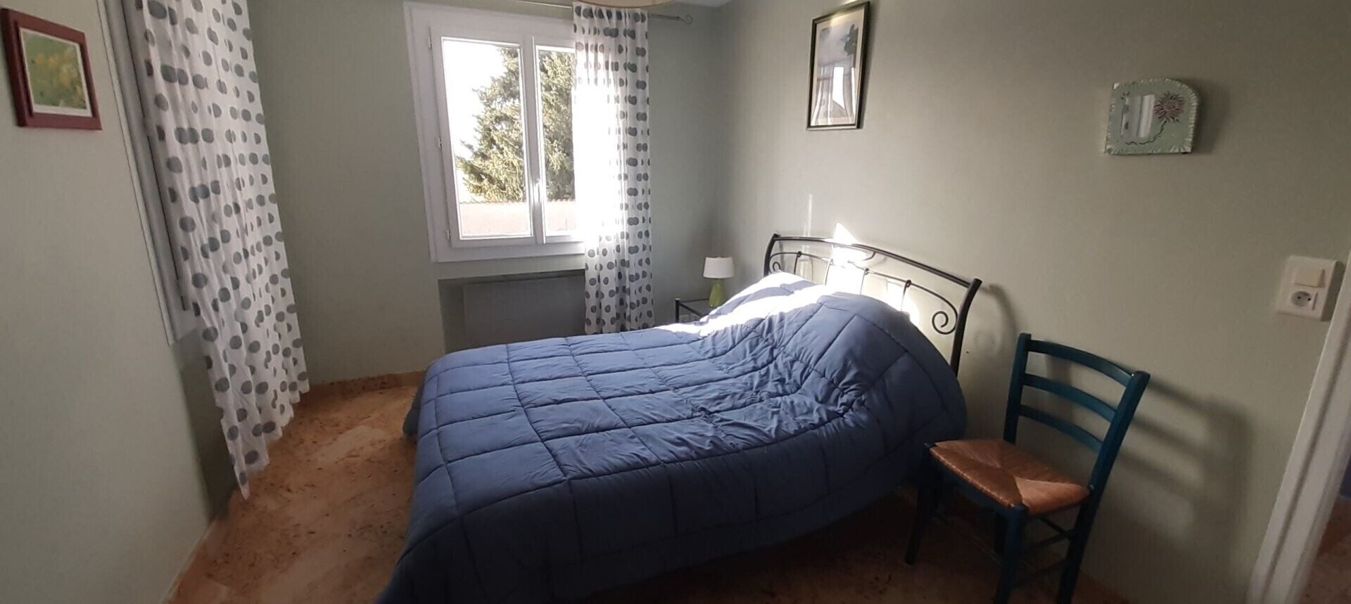 A bedroom with a bed, a chair, a window, and a wall with a picture.