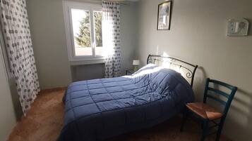 A bedroom with a bed, a chair, a window, and a wall with a picture.