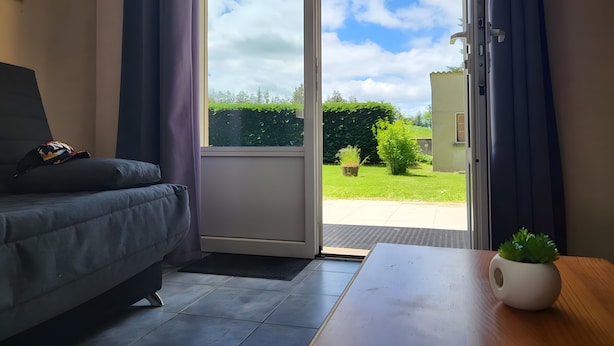 A room with a sofa, a table with a plant, and a sliding glass door leading to a garden. - Holiday Home “La Maison De Charlotte” in Lespéron, Ardèche (Lespéron)