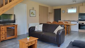 A living room with a sofa, TV, wooden cabinet, and a small table. There's a staircase leading to another level. - Holiday Home “La Maison De Charlotte” in Lespéron, Ardèche (Lespéron)