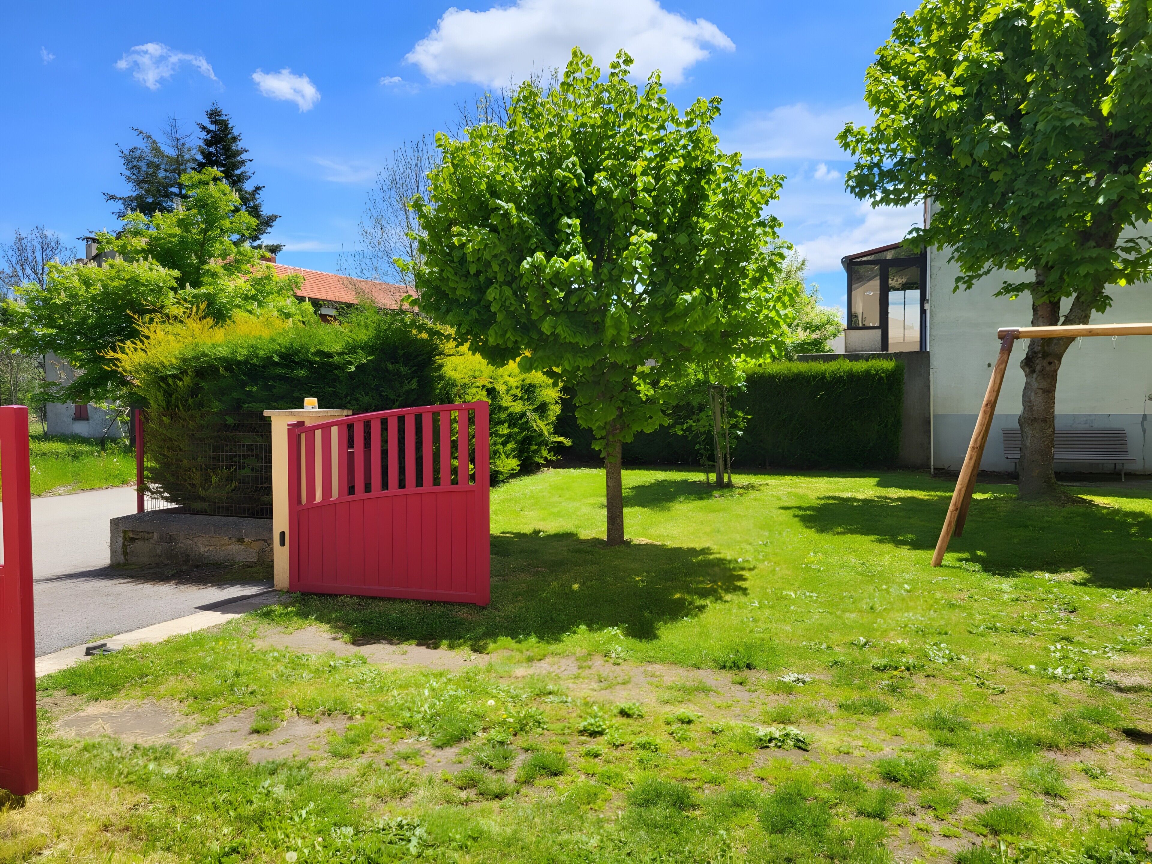 A residential yard with a red gate, a swing set, and a tree.