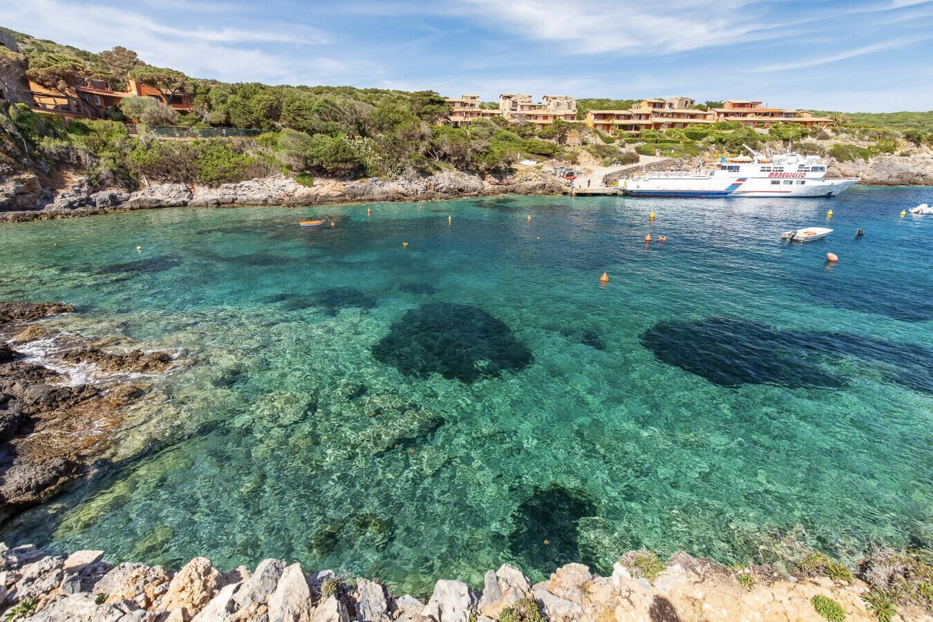 Una zona costiera con acque cristalline, un litorale roccioso e una barca chiamata 'BARREGGIO' sullo sfondo.