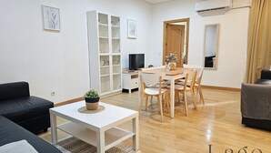 Ein modernes Wohnzimmer mit Essbereich, einem schwarzen Sofa, einem weißen Couchtisch und einem Fernseher.