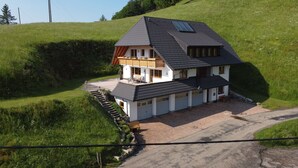 A two-story house with a sloped roof, a balcony, and a paved driveway. - Vacation apartment 'Wiesenpanorama' (Münstertal/Schwarzwald)