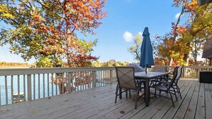 Une terrasse en bois avec une table et des chaises, donnant sur une étendue d’eau et entourée d’arbres aux feuilles d’automne.
