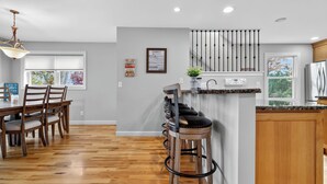 Une cuisine moderne avec un plancher en bois, un coin repas avec une table et des chaises, et un bar avec des tabourets.