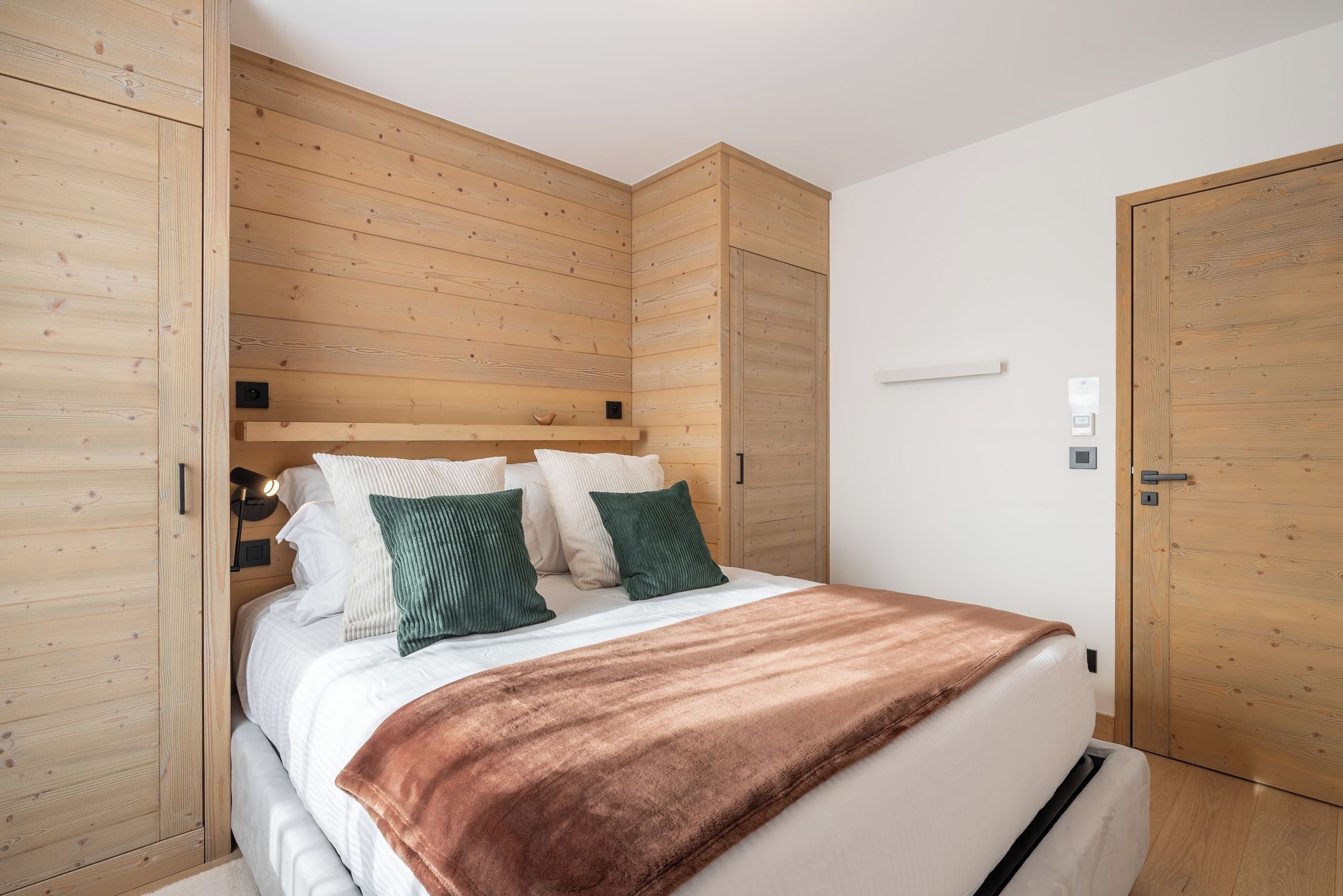 A bedroom with a wooden headboard, a bed with white bedding and a brown blanket, and wooden wardrobes.