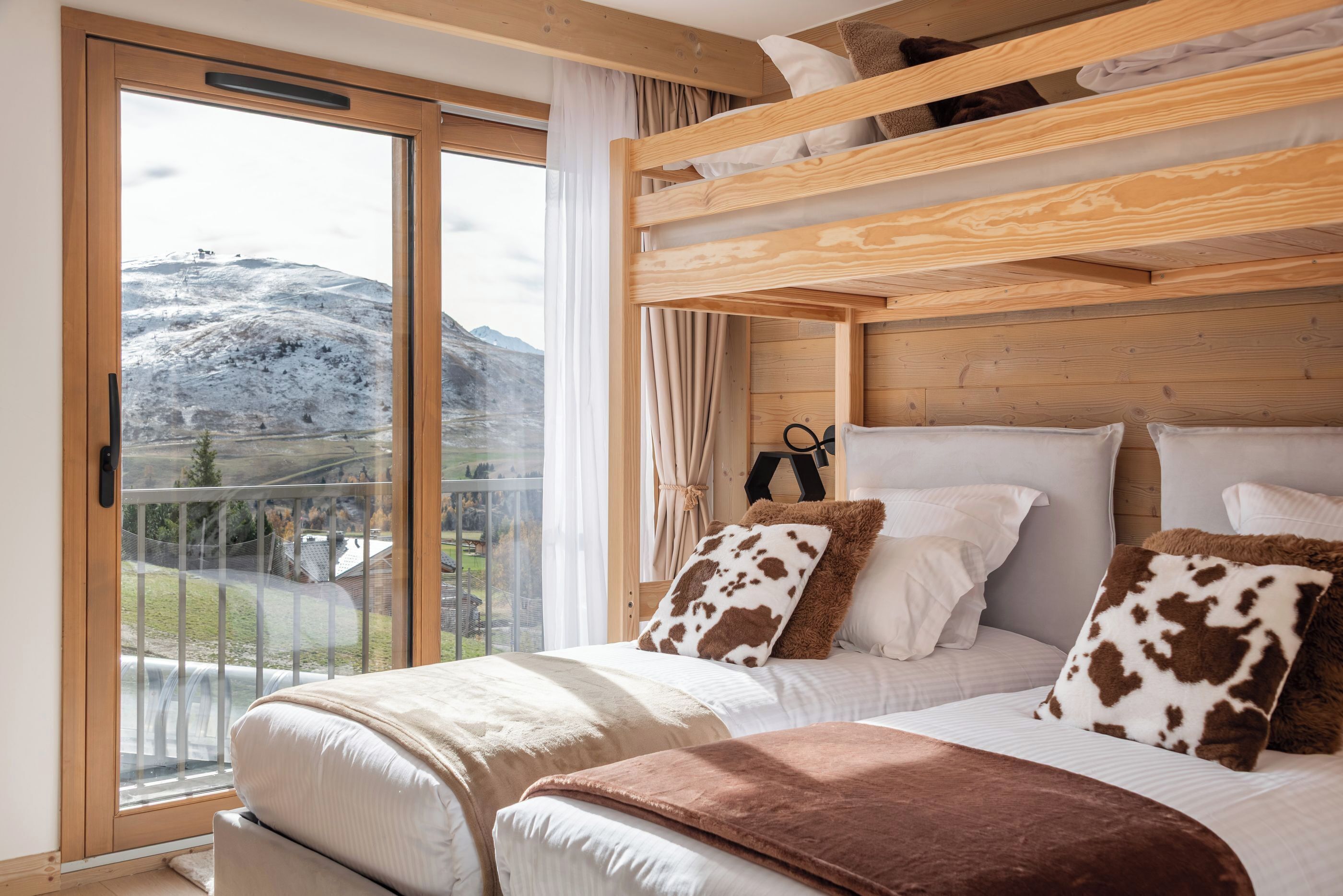 A bedroom with a bunk bed, a large window with a view of a snowy mountain, and a balcony.