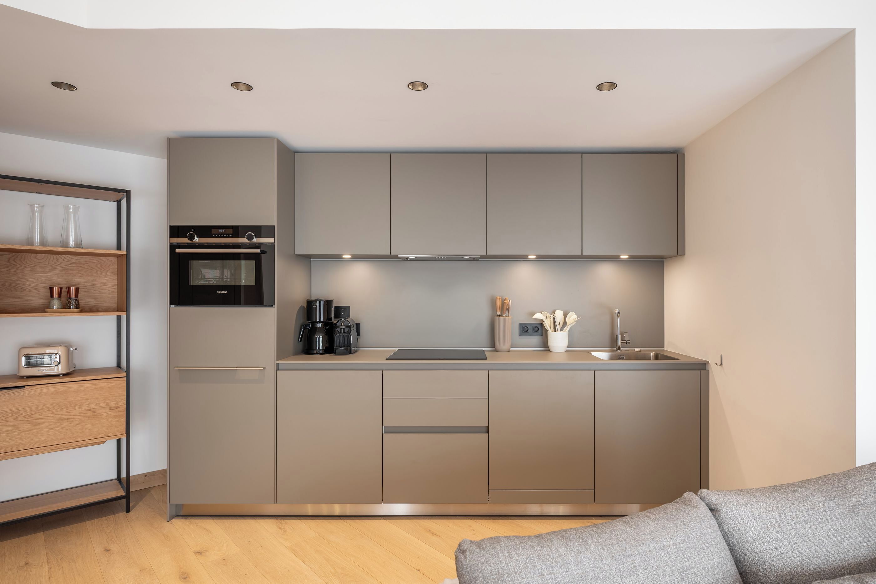 Une cuisine compacte dotée d’appareils électroménagers intégrés, d’un petit plan de travail et d’une étagère en bois.
