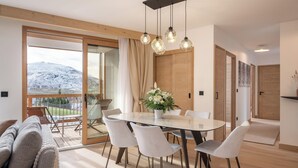 Uma sala de jantar moderna com mesa de vidro, cadeiras brancas e teto de madeira.