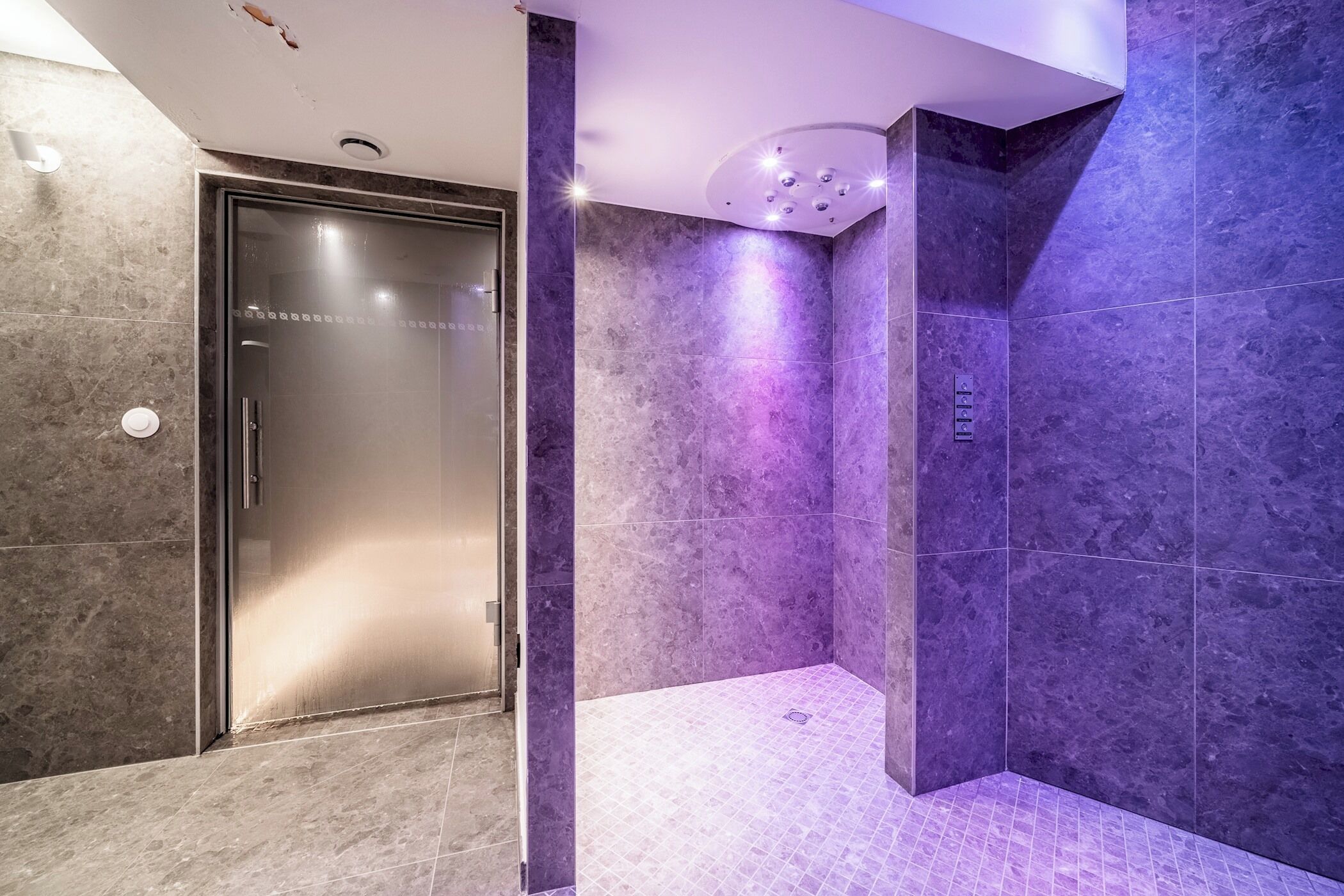 Un baño moderno con cabina de ducha de vidrio, paredes de mármol y suelo de baldosas.