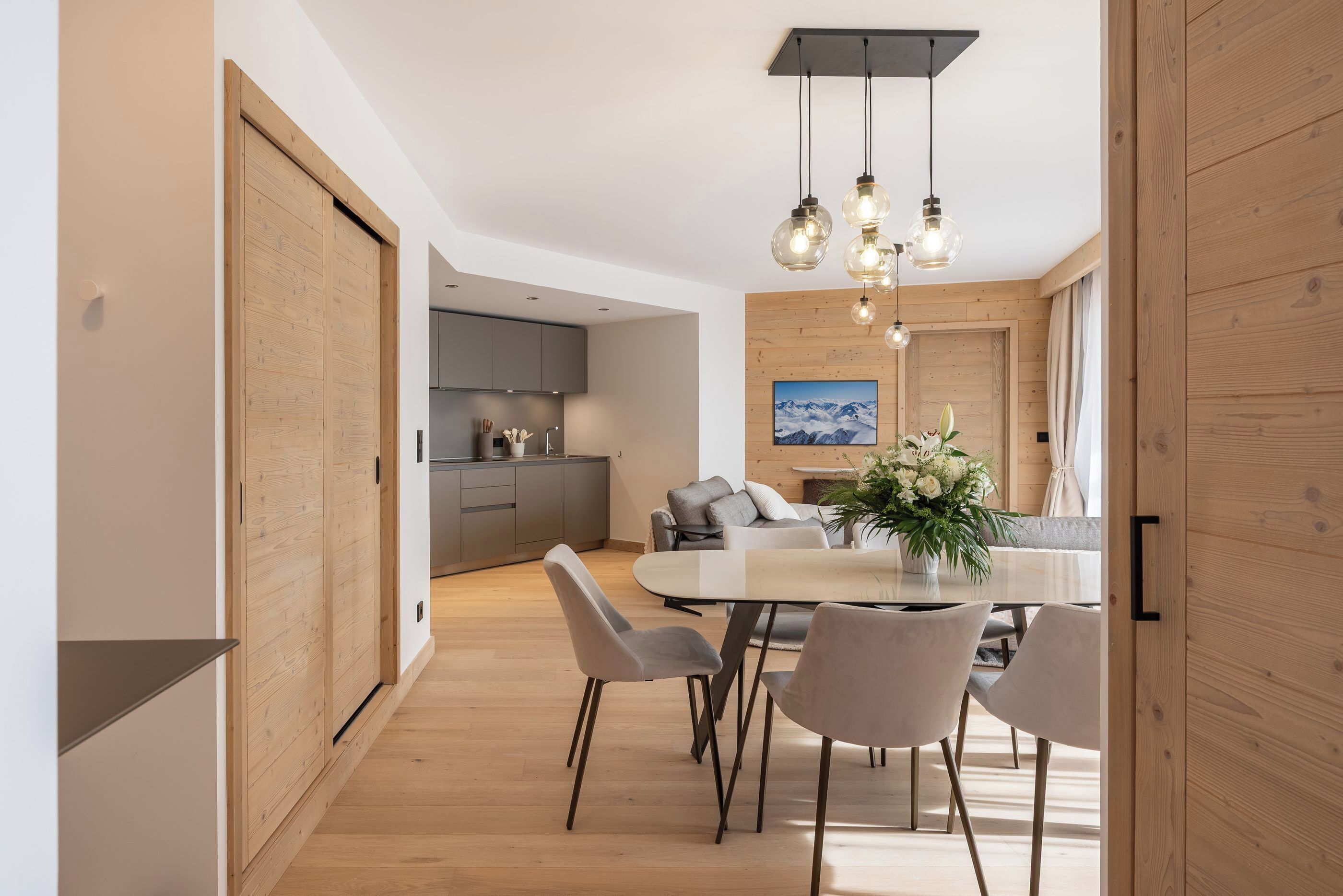 A modern kitchen with a central island, wooden sliding doors, and a dining area with a table and chairs.
