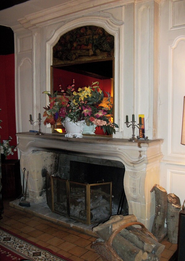 A fireplace with a floral arrangement, candles, and a mirror above it. - le relais cicero (La Flèche)