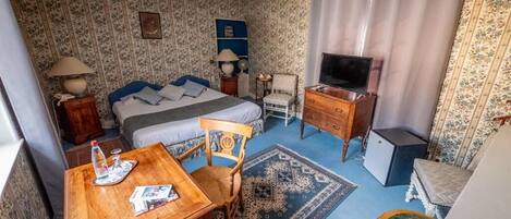 A hotel room with a bed, a desk with a chair, a television, a dresser, and a small table with a chair.