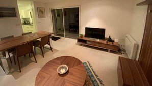 A modern living room with a wooden dining table, a TV on a wooden stand, and a sliding glass door leading to a balcony. - ★ House 49m2 ★ Pessac ★  Netflix ★ Bus ★ Train (Pessac)