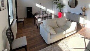 A spacious living room with a white sofa, wooden flooring, a dining area with chairs, a large window, and a hanging light fixture. - ★ House 92m2 ★ Pessac ★ Netflix ★ Bus ★ Train (Pessac)