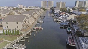 A marina with boats docked along a canal, surrounded by residential buildings and a large hotel in the background. - Walk to the Beach or the Bay! (Ocean City)