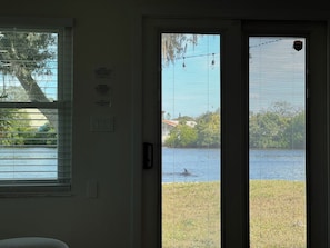 A room with a door leading to a view of a lake, a window with blinds, and a wall-mounted sign. - Waterfront Experience | Boatlift & Boat Rental (Tarpon Springs)