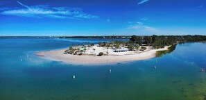 An aerial view of a coastal property with a sandy beach, clear blue waters, and a small island with structures. - Waterfront Experience | Boatlift & Boat Rental (Tarpon Springs)