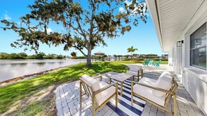 A patio with outdoor furniture, a tree, and a view of a body of water. - Waterfront Experience | Boatlift & Boat Rental (Tarpon Springs)