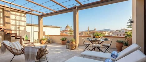 Une terrasse extérieure ensoleillée, dotée de meubles en osier, d’une table à manger et de fauteuils de détente.
