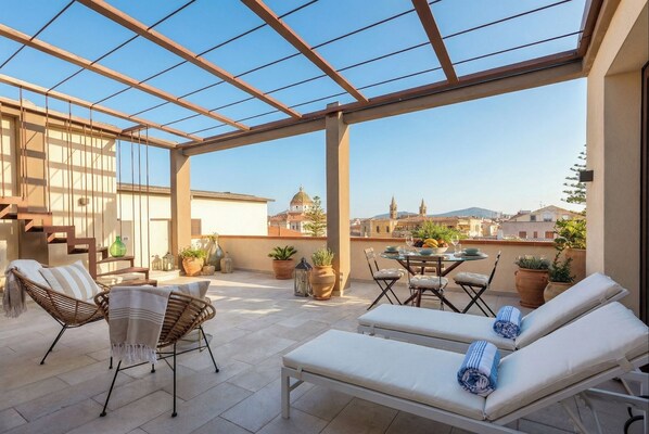 A sunlit outdoor patio with wicker furniture, a dining table, and lounge chairs. - ClickSardegna San Michele Penthouse with Terrace and Parking in the City Center (Alghero)