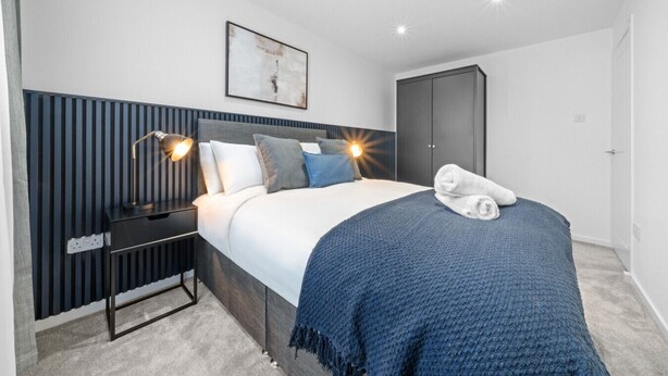 A modern bedroom with a bed, bedside lamps, a headboard, a wardrobe, and a painting on the wall. - Linden House - 3 bed home in Hamilton (Hamilton)