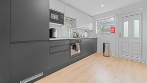 A modern kitchen with grey cabinets, a built-in oven, and a window with a view of trees. - Linden House - 3 bed home in Hamilton (Hamilton)
