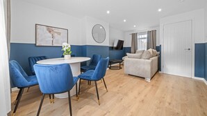 A modern living room with a round table, blue chairs, a sofa, and a TV. - Linden House - 3 bed home in Hamilton (Hamilton)
