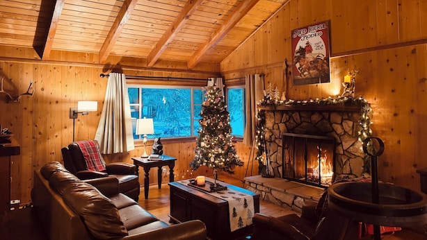 Ein gemütliches Blockhauss-Interieur mit Kamin, Ledersofa, Weihnachtsbaum und Holzwänden.