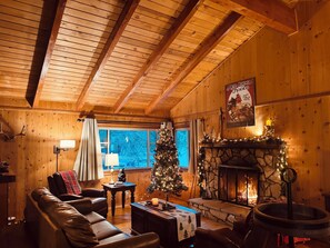 Ein gemütliches Blockhauss-Interieur mit Kamin, Ledersofa, Weihnachtsbaum und Holzwänden.