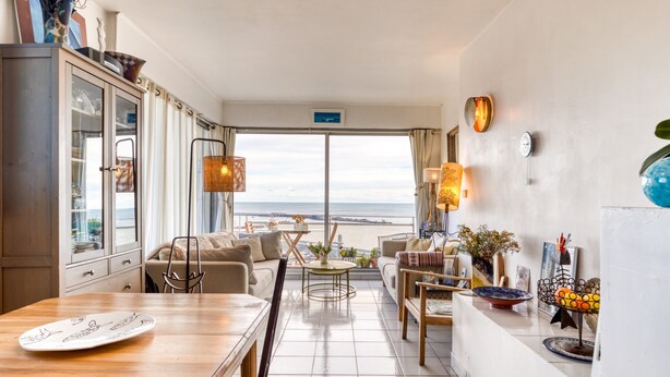 Une cuisine moderne avec vue sur la mer, un coin repas avec une table en bois et un espace salon confortable avec un canapé et des fauteuils.