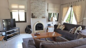 Ein Wohnzimmer mit Fernseher, Sofa, Couchtisch, Kamin und großen Fenstern.