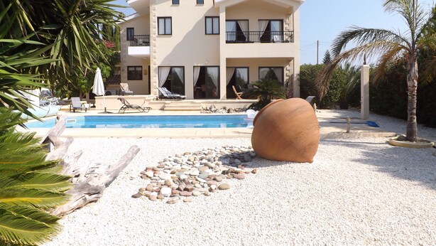 Ein zweigeschossiges Haus mit Swimmingpool, umgeben von Kies und Palmen.