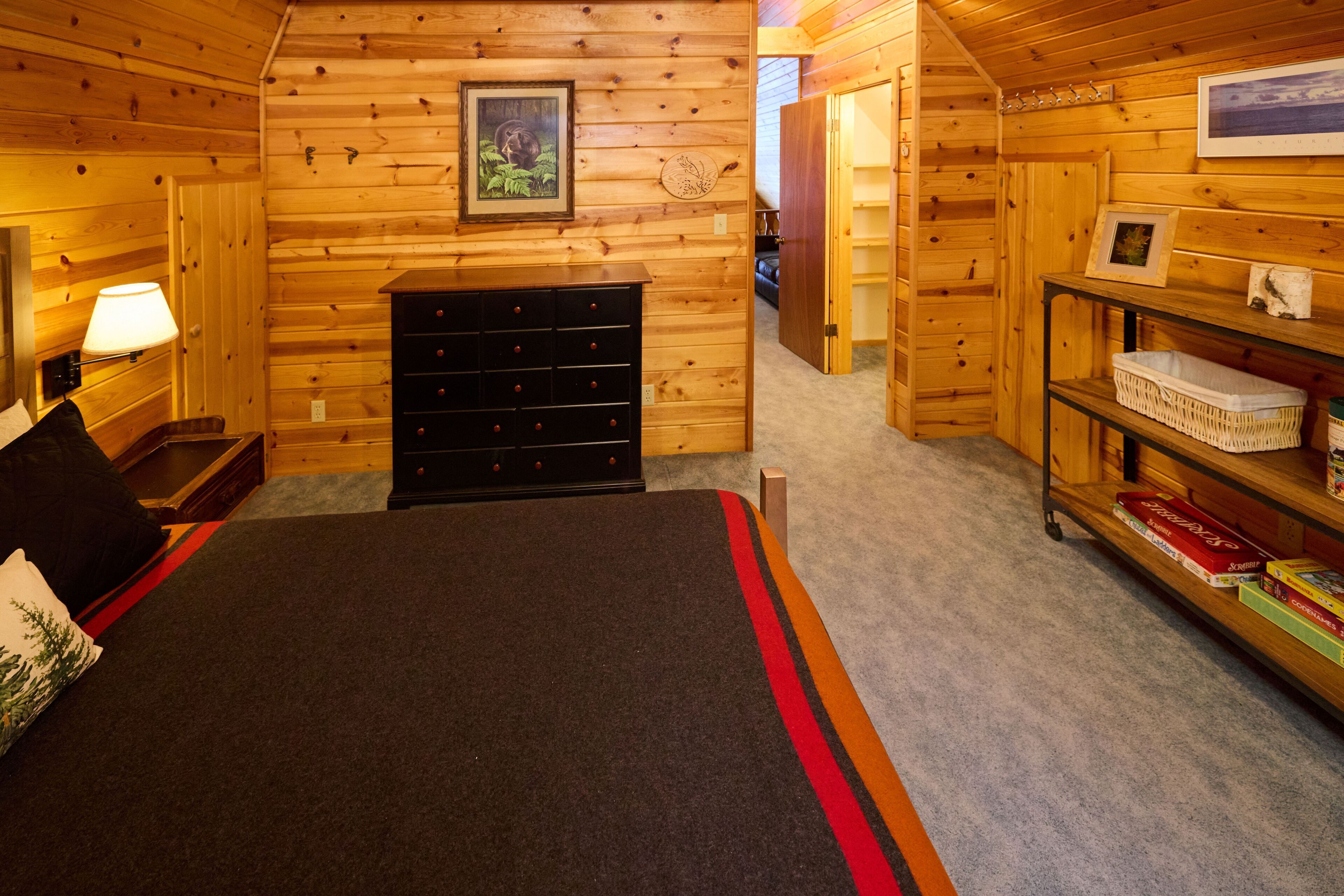 Ein gemütliches Schlafzimmer in einer Blockhütte mit einem Bett, einem Schminktisch und Regalen mit Büchern und Dekoration.