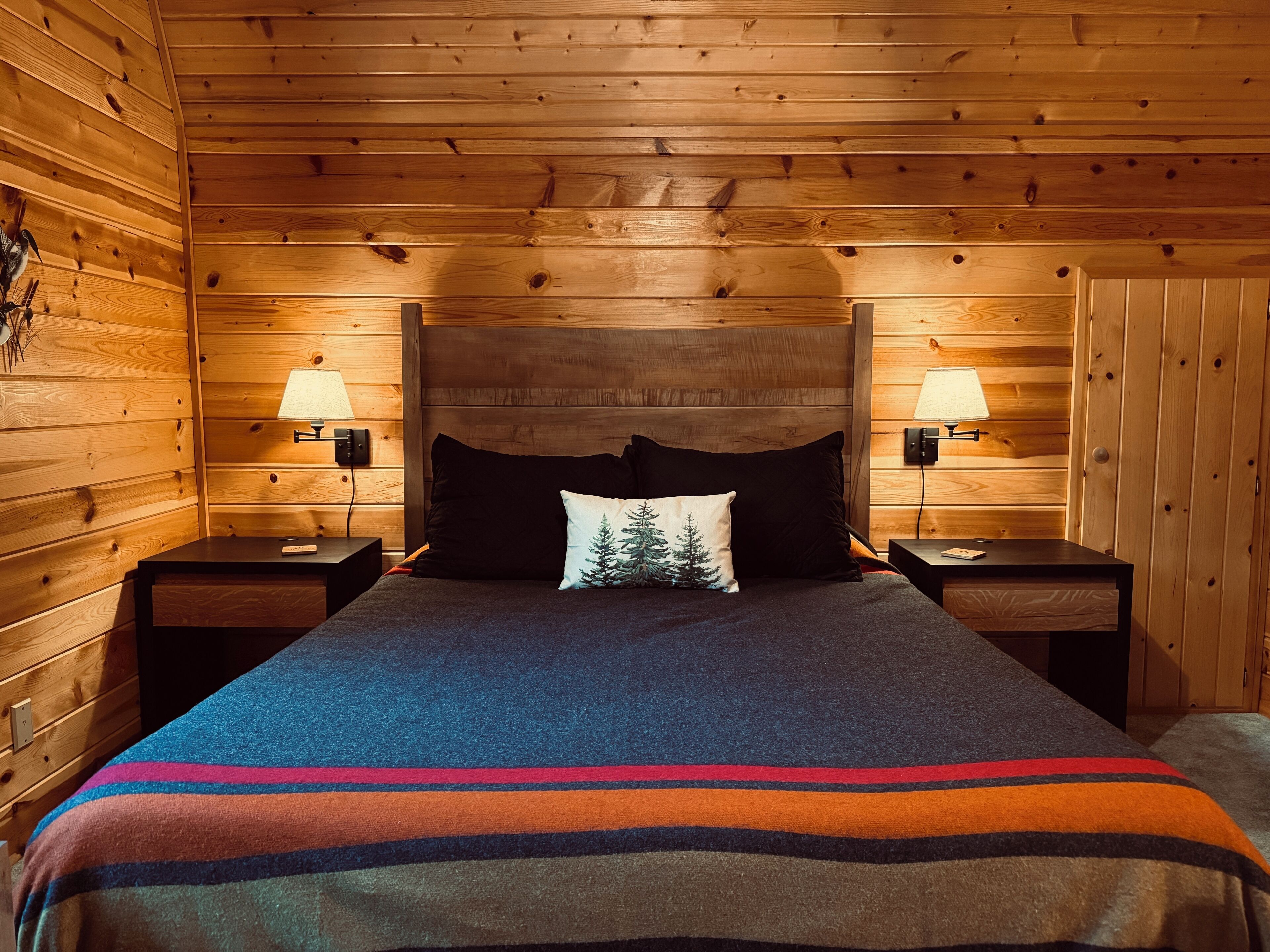 A wooden cabin room with a bed, two nightstands, and two wall-mounted lamps.