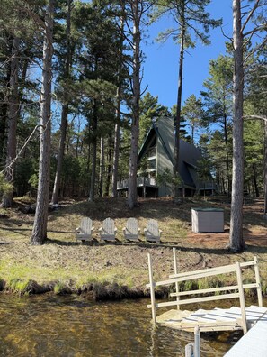 Eine Hütte, umgeben von hohen Kiefern, mit einem Steg und einem kleinen Schuppen.