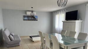 A modern living room with a glass dining table, white chairs, a grey sofa, a mounted TV, and a painting on the wall. - Gîte des 3 Moulins - A haven of tranquillity in the heart of the vineyards (Gornac)
