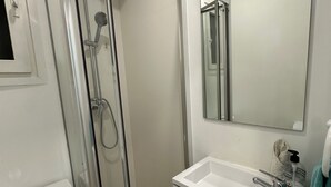 A modern bathroom with a glass-enclosed shower, a white sink with a mirror above it, and a towel hanging on the wall. - C (Barcelona)