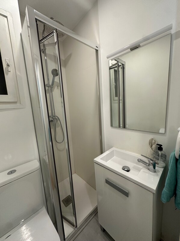 Un bagno moderno con cabina doccia in vetro, un lavandino bianco con specchio sopra e un asciugamano appeso al muro.