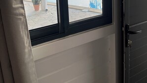 A room with a window overlooking a pool area, a door, and a potted plant. - Coco Banana - Superior bungalow - pool view (Baie-Mahault)