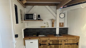 A compact kitchen with a white refrigerator, wooden cabinets, a sink, and a small dining area with a chair and table. - Coco Banana - Superior bungalow - pool view (Baie-Mahault)