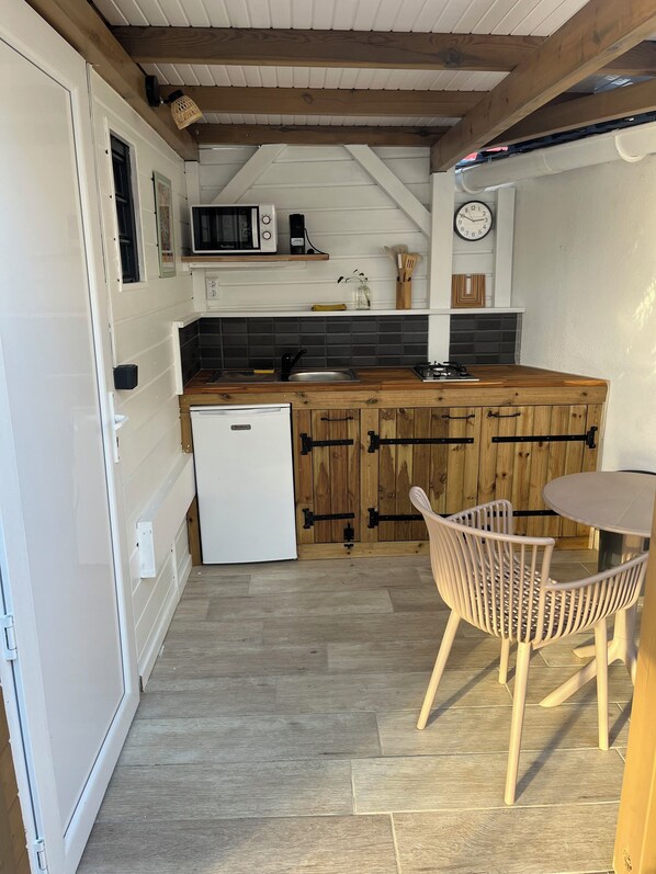 Eine kompakte Küche mit einem weißen Kühlschrank, Holzschränken, einem Spülbecken und einer kleinen Essecke mit Stuhl und Tisch.