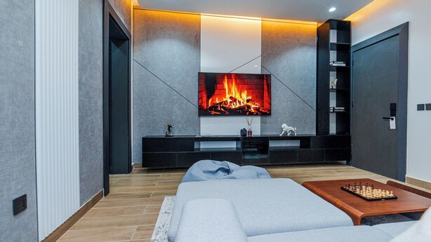 A modern living room with a large flat-screen TV, a fireplace, a sofa, and a chessboard.