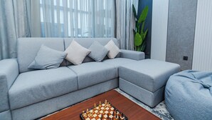 A modern living room with a grey sectional sofa, a wooden coffee table with a chessboard, and a large green plant.
